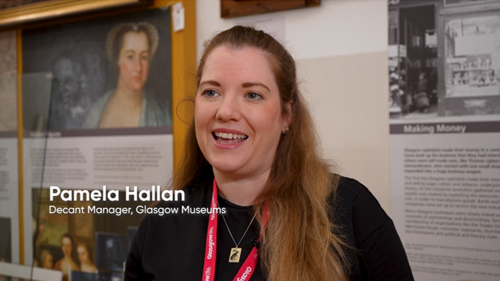 A person with long auburn hair being interviewed in a museum with paintings behind them