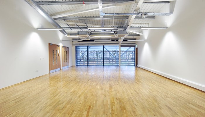 an empty rooms with windows at the end. The floor has a wooden effect and the walls are white