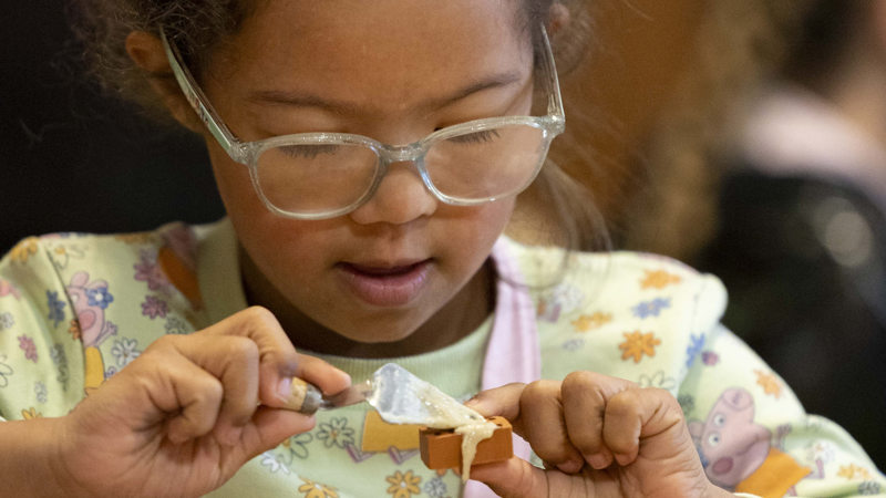 A young girl wearing glasses is concentrating on a craft project