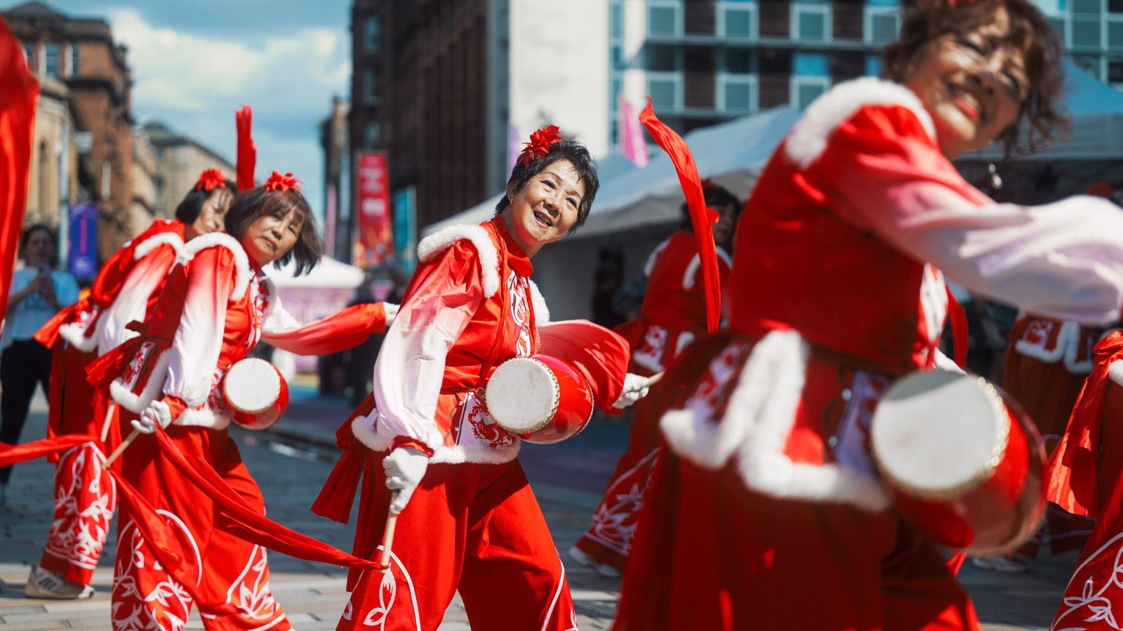 Musical performers wearing red and white costumes play the drums on a city street