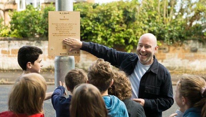 A man and a group of children stand in front of Gaelic language signage