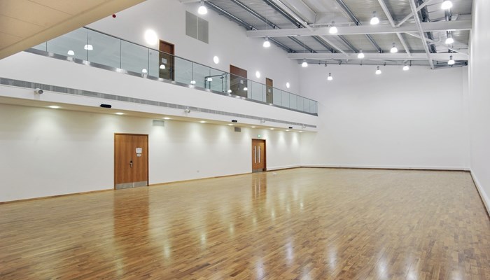 an empty sports hall with white wall and a wooden floor. there is a spectator floor to the left