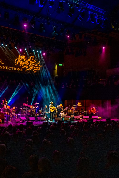 Musicians on a stage with multicoloured stage lights. The words Celtic Connections are displayed in the concert hall.
