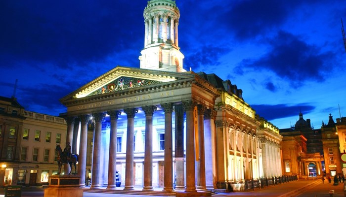 night exterior shot of GoMA showing the classical frontage illuminated by spotlights and a blue sky above