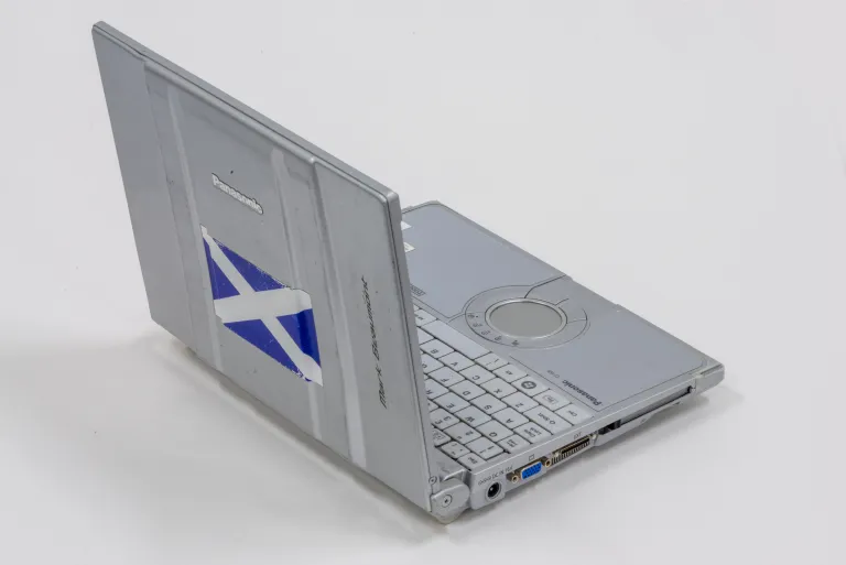 a photograph of a grey laptop. On the lid, there is a Scottish flag sticker.