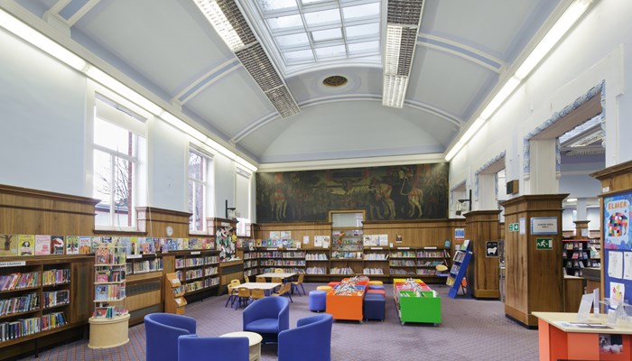 Spacious and colourful children's area  There are tables and chairs in the middle of the area, wood panelling a third of the height of the walls and a high curved ceiling with a long rectangular, colonial-style skylight. From this angle you can see the mural of 'Queen Mary at the Battle of Langside'