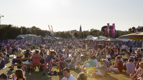 A large crowd of people sitting in the Glasgow Green fan zone during the 2014 Commonwealth Games on a sunny evening.