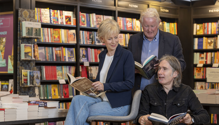 Two men and a woman smile at each other in a library setting, with books in the background and foreground