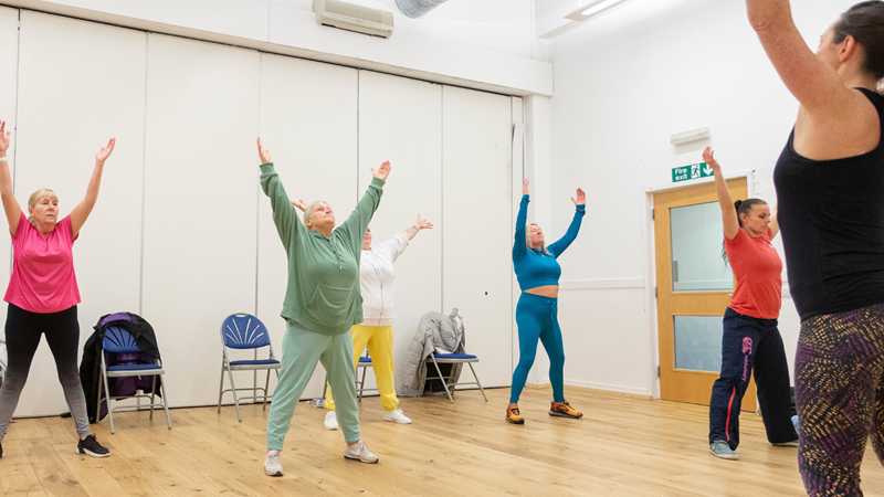 A group of people and an instructor with their hands in the air while taking part in a wellbeing class