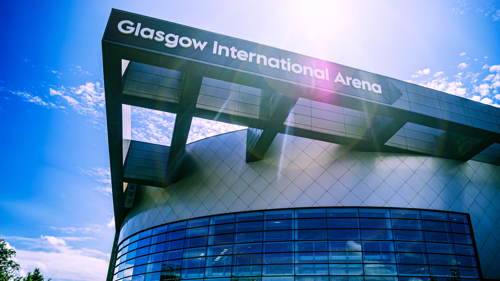 Glasgow International Arena exterior with curved glass frontage and signage beneath a bright sunlit sky.