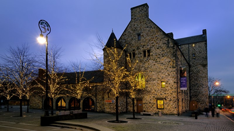 Photograph showing St Mungo Museum illuminated by lights on trees outside, as seen from Glasgow Cathedral.