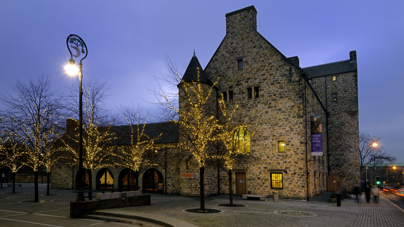 Photograph showing St Mungo Museum illuminated by lights on trees outside, as seen from Glasgow Cathedral.