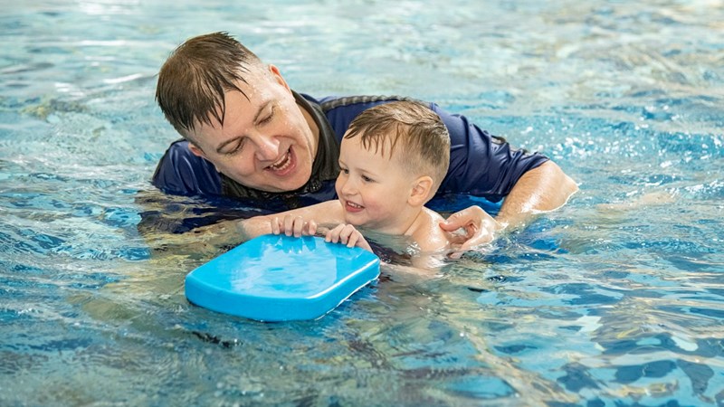 A swimming coach helping a child in the pool who is holding a float