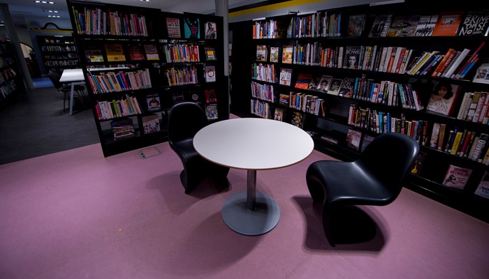 small white round table with black curved modern chairs. There are black bookshelves beside it.