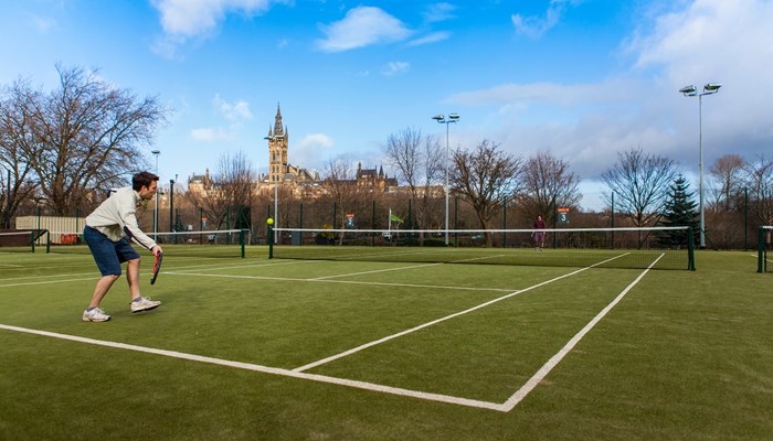 A person hitting a tennis ball on the courts at Kelvingrove Park