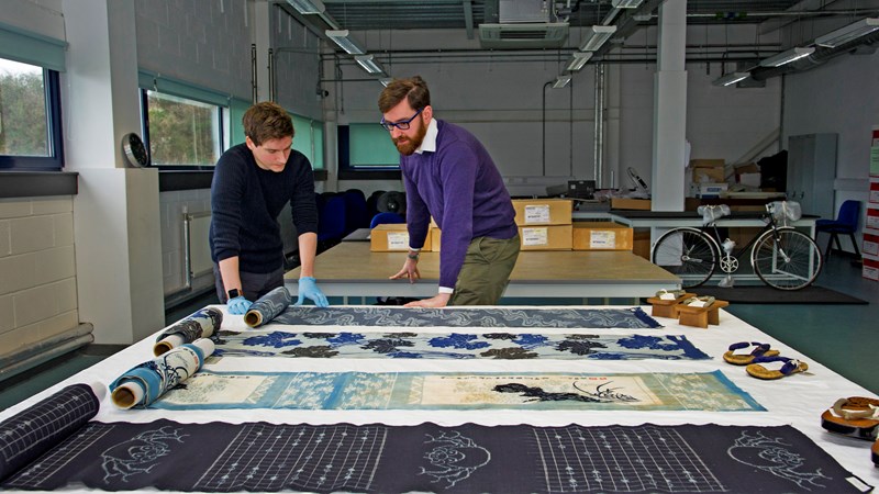 Two curators at work in the Research Room at GMRC viewing textile objects laid flat on a table