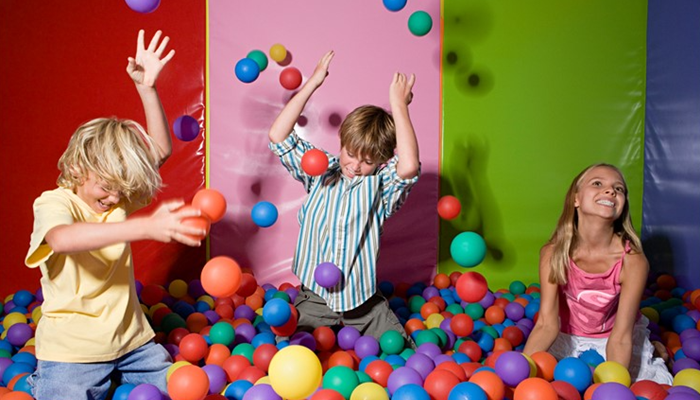 3 children playing in a ball pit throwing colourful balls into the air 