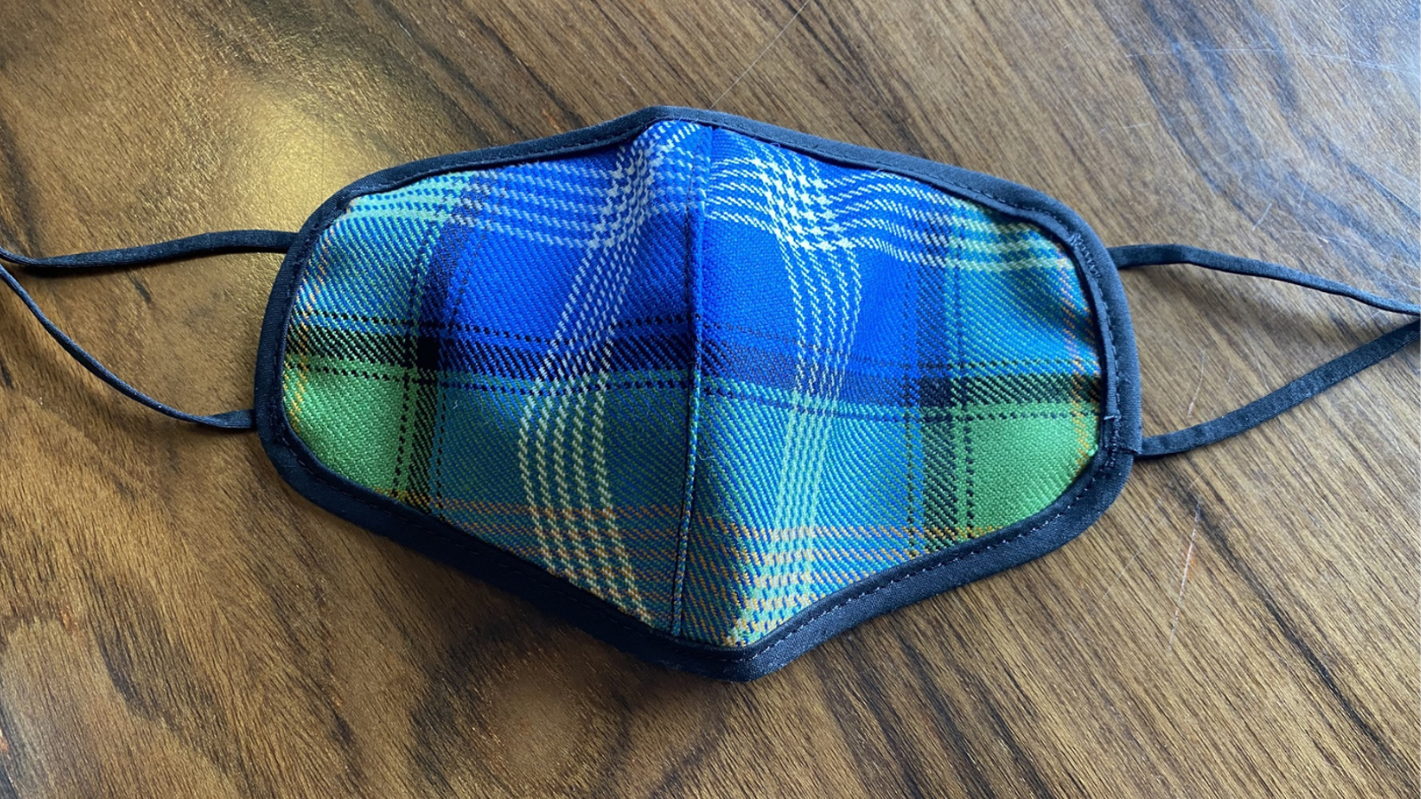 Reusable fabric face mask made from Islamic Tartan patterned material, resting on a wooden surface.