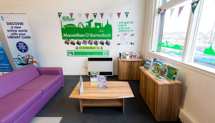 A corner-room meeting area for health and wellbeing support such as Macmillan Cancer support. There is a purple sofa, a wooden table and cupboards.