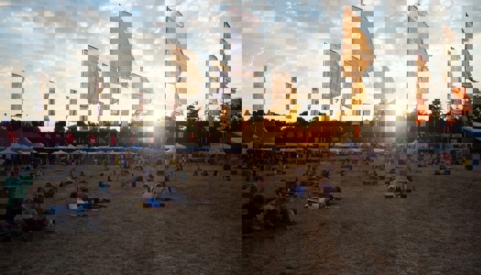 Music fans enjoy a festival as multicoloured flags fly above and the sun goes down