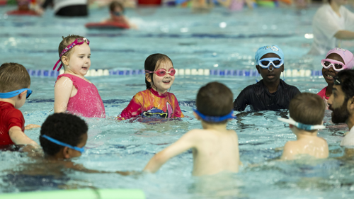 A group of young people taking part in a swimming lesson in a pool. They are holding hands and swimming in a circle