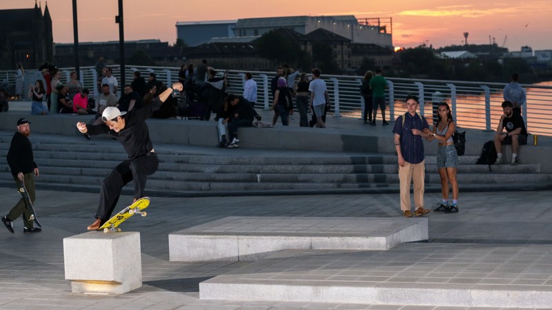 A skateboarder performs a trick as a crowd watches on and the sun sets in the background
