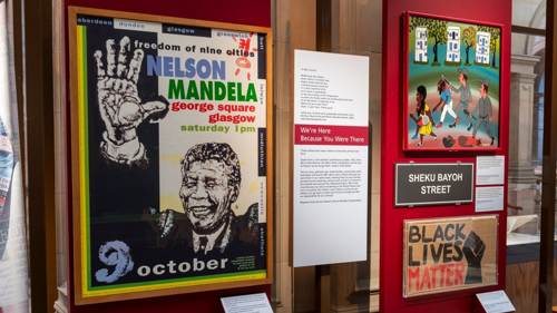 A collection of posters and artwork displayed as part of a museum exhibit including a Nelson Mandela poster and Black Lives Matter placard