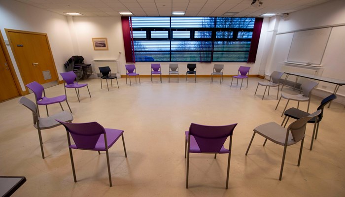 Chairs are set out in a circle in a room with a wooden floor. There is a window in the background.