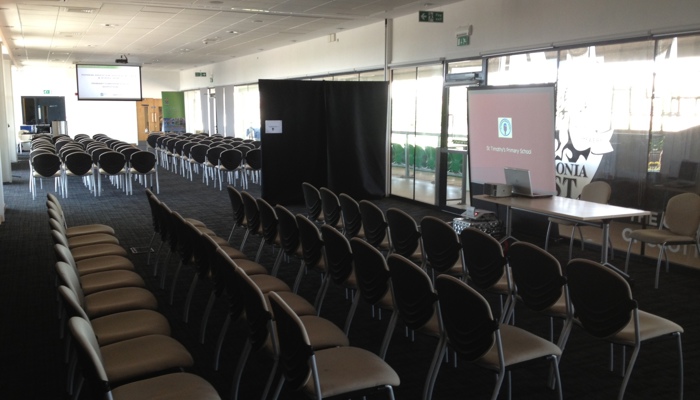 a meeting room with rows of chairs and a screen and projector to the right of the image