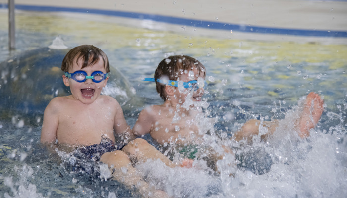 Two young boys smiling and laughing while they splash in the water in a swimming pool