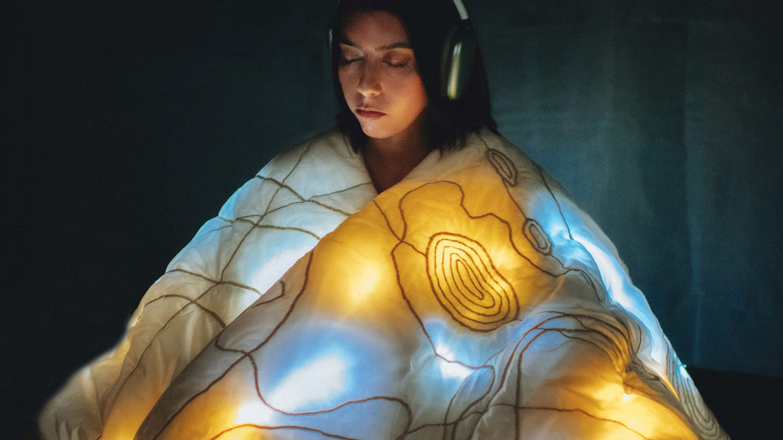 A person wearing headphones is wrapped in an illuminated cape