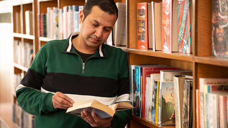 Person looking at a book and leaning against a bookshelf in Knightswood library