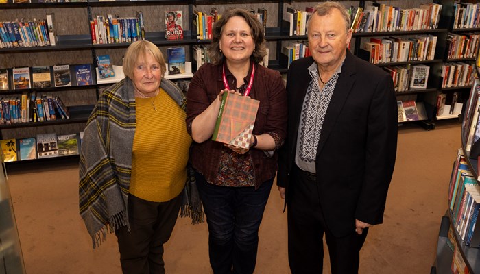 Special Collections Librarian, Susan Taylor at The Mitchell Library holding a copy of Robert Burns: Selected Works, she is standing in the middle of the two authors of the book, Hanna Dyka and Dr Peter Kormylo