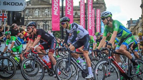A large group of people competing in a cycling road race in a city centre
