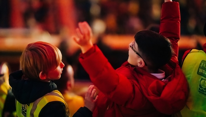 Close-up of two young children in a concert audience, one wearing a high-vis vest, reaching their hands up in excitement.