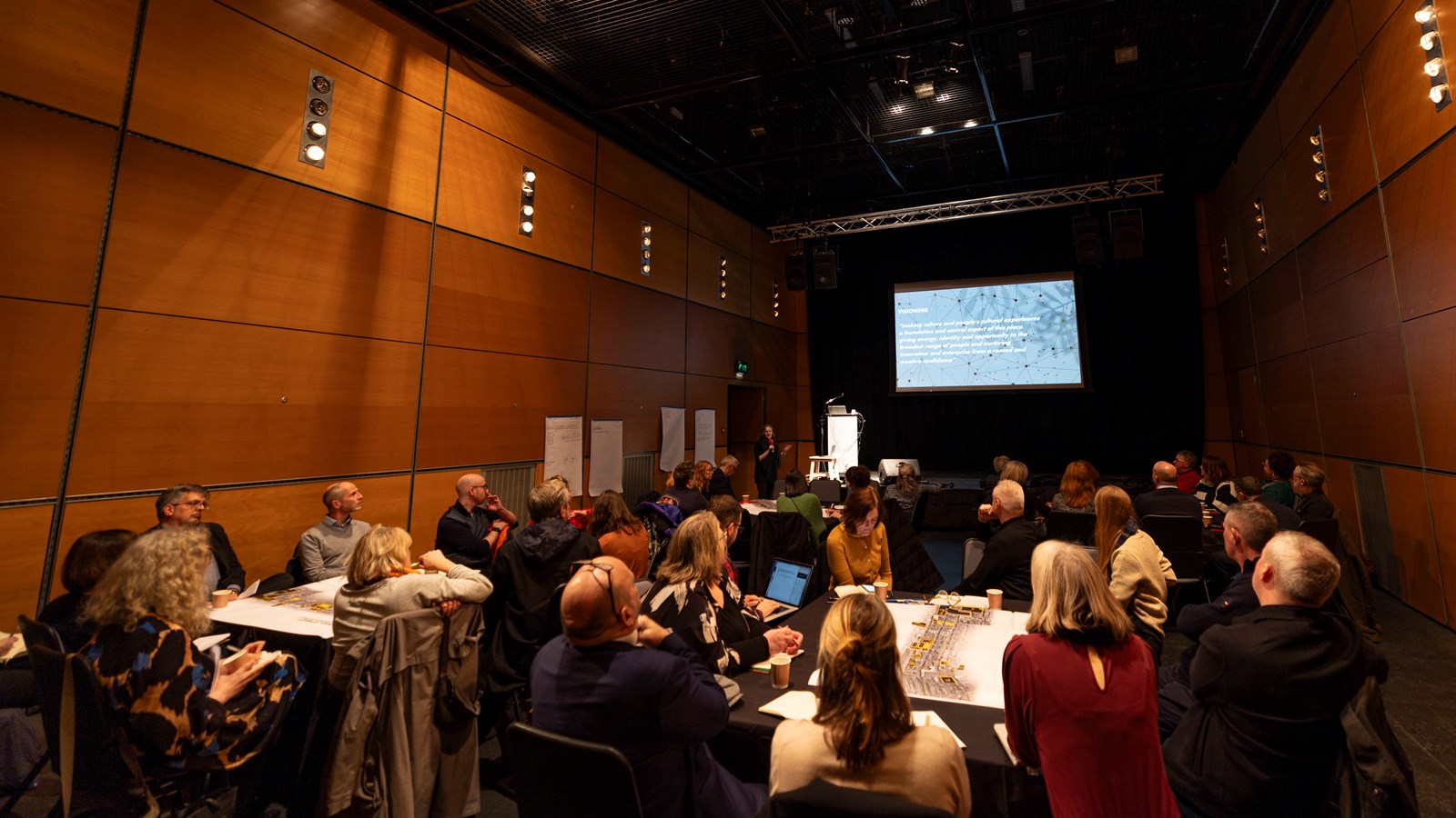 Groups of people sitting down at tables look at a PowerPoint screen during a workshop at the Centre for Contemporary Arts on Sauchiehall Street.