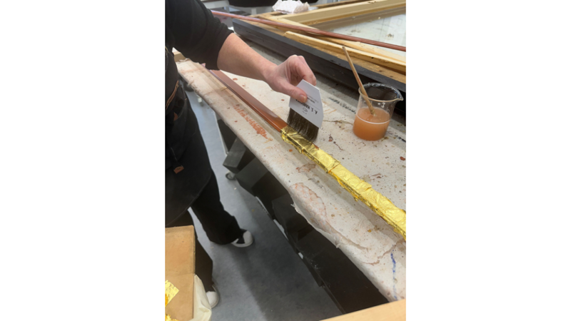 close up of hands gilding using gold leave on a wooden frame in a workshop setting