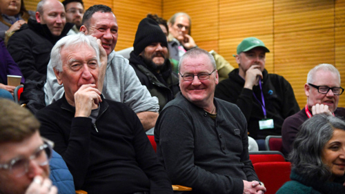 Close up of a group of smiling audience members sitting on tiered seating at a panel discussion event