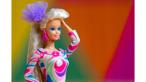 Barbie doll posed wearing a brightly coloured abstract dress against a bright abstract background.