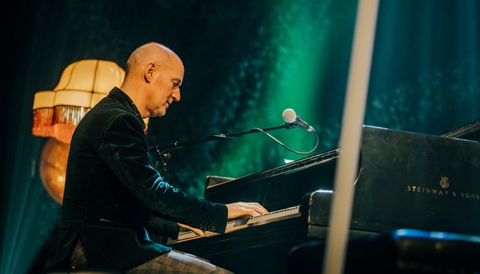 A person in a dark suede jacket playing piano onstage