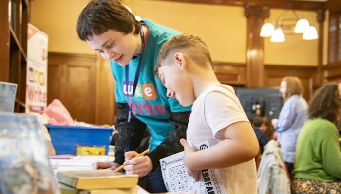 Volunteer helps a child with an activity sheet at a library event.