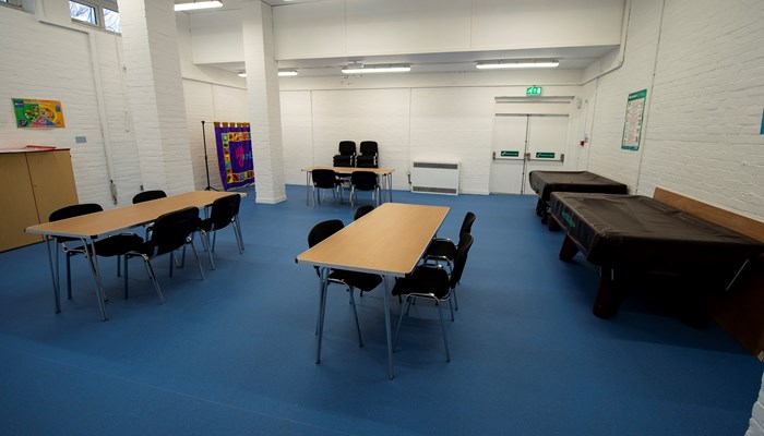 a room with three tables with chairs around them. the carpet is blue and the walls are white. there are windows high up in the room and its is lit by fluorescent lights