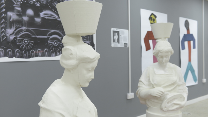 Two statues of "mother Glasgows" are displayed on red pallets. In the background there are painting and prints. 