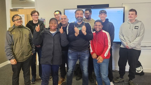 A group of ten students standing in a classroom celebrating the award that one of them is holding up