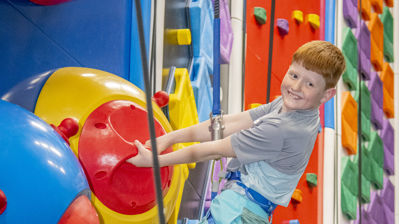 Boy climbing a colourful indoor wall.