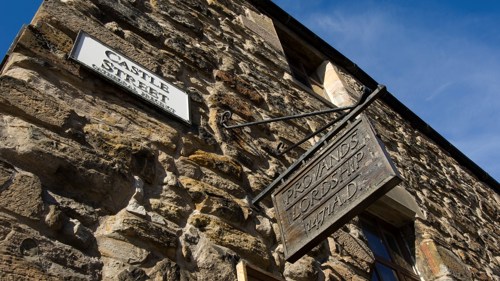 Close up on the stone wall of an old building with a metal hanging sign that reads Provands Lordship