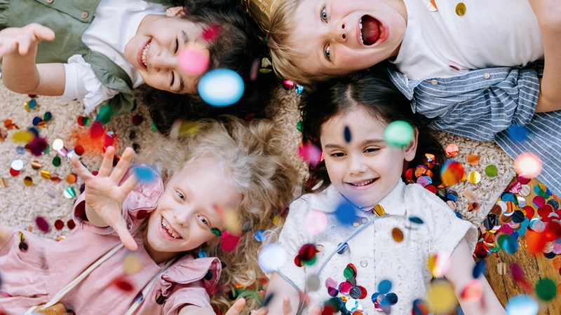 Fur young kids lying on the floor laughing with multi-coloured confetti falling on them