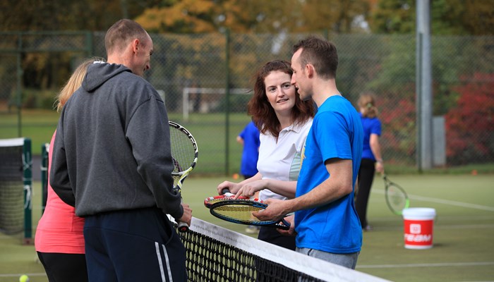 Four people speaking to each other at the net on a tennis court