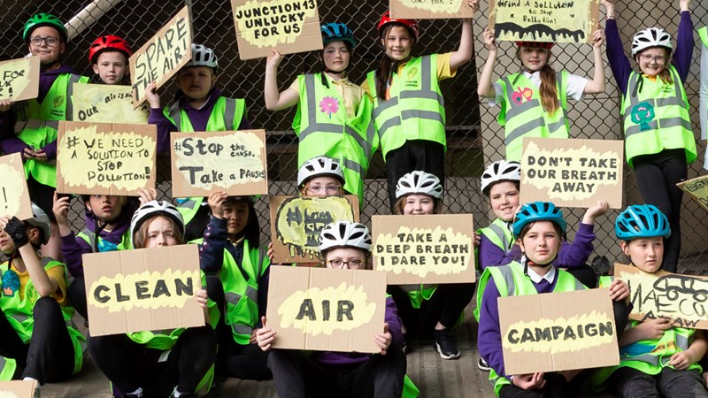 Children in cycling helmets pose together holding a variety of anti-pollution signs 