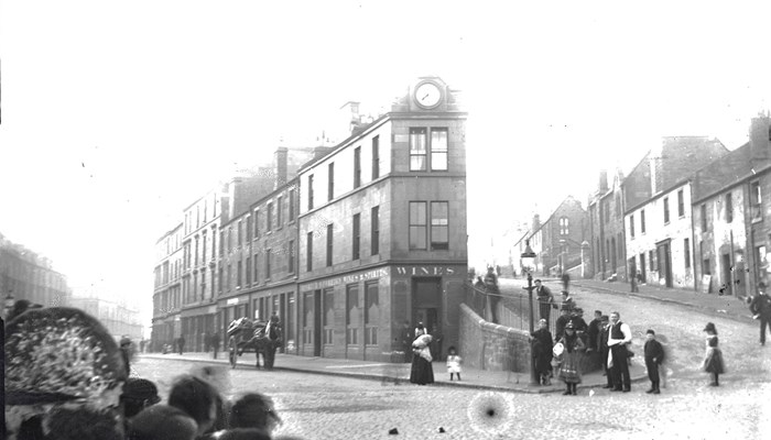 An old building at the bottom of two slopes. People standing on the road